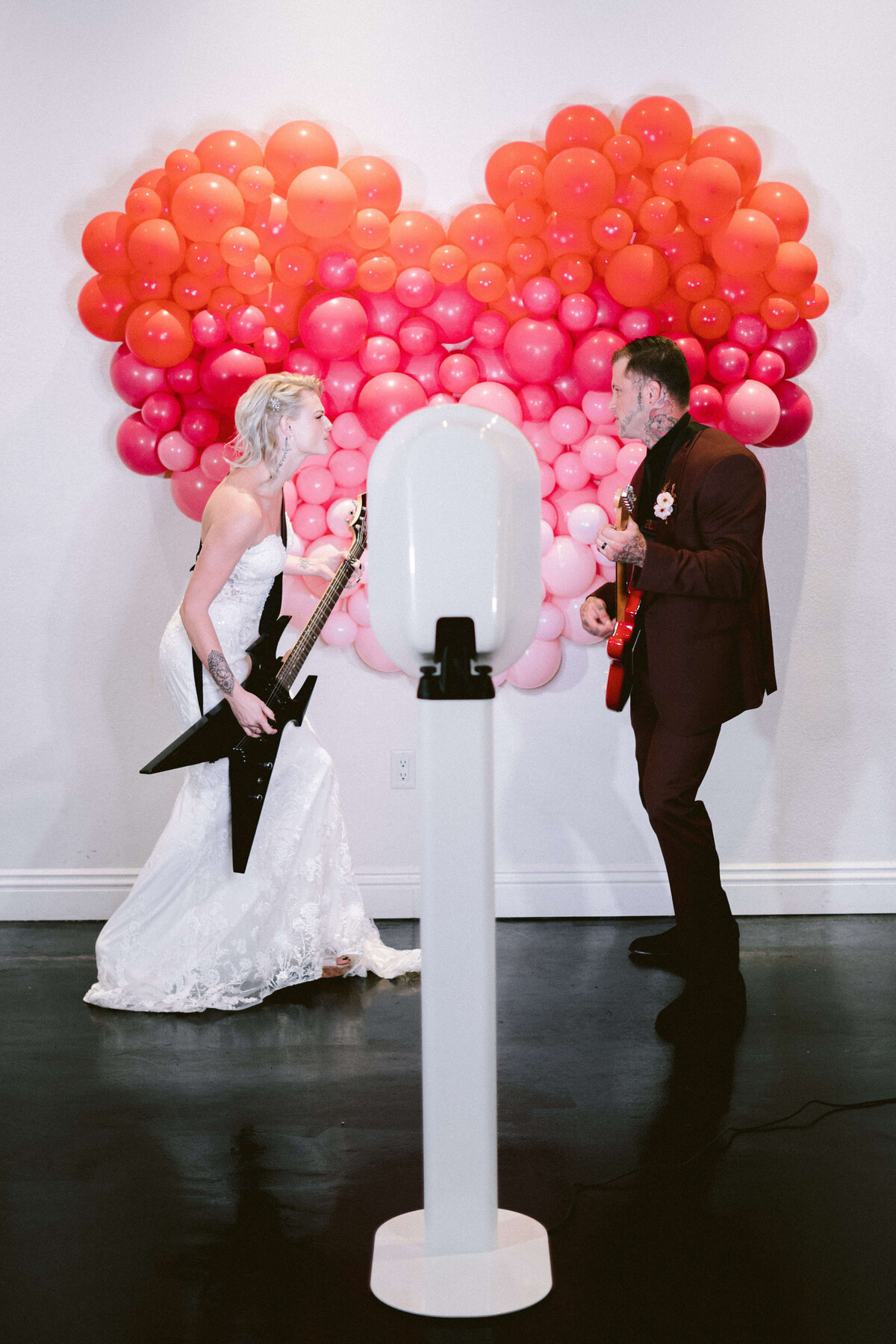 Bride and groom holding a guitar as a props for their photo booth picture with colorful heart shaped balloon backgrounf