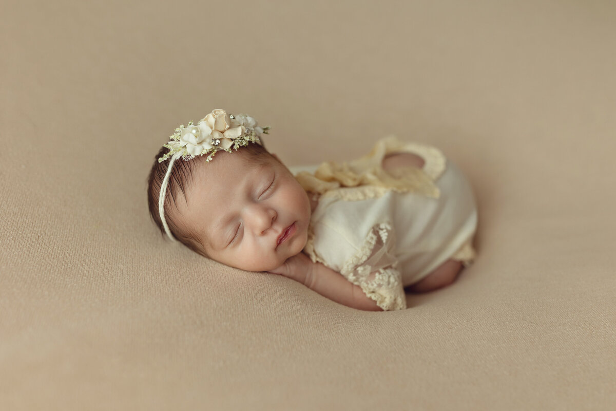 A sleeping newborn baby girl in a yellow dress and matching floral headband