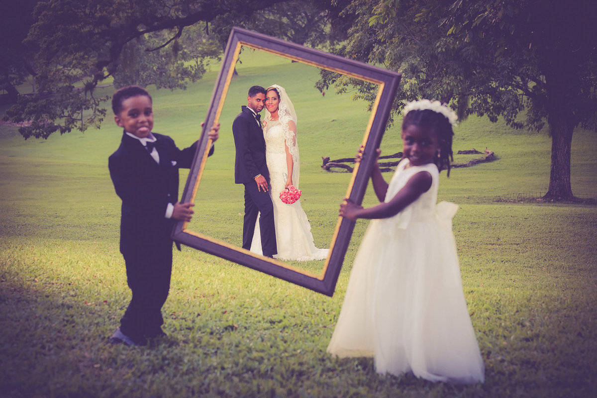 Bride and groom through picture frame held by ring bearer and flowergirl. Photo by Ross Photography, Trinidad, W.I..