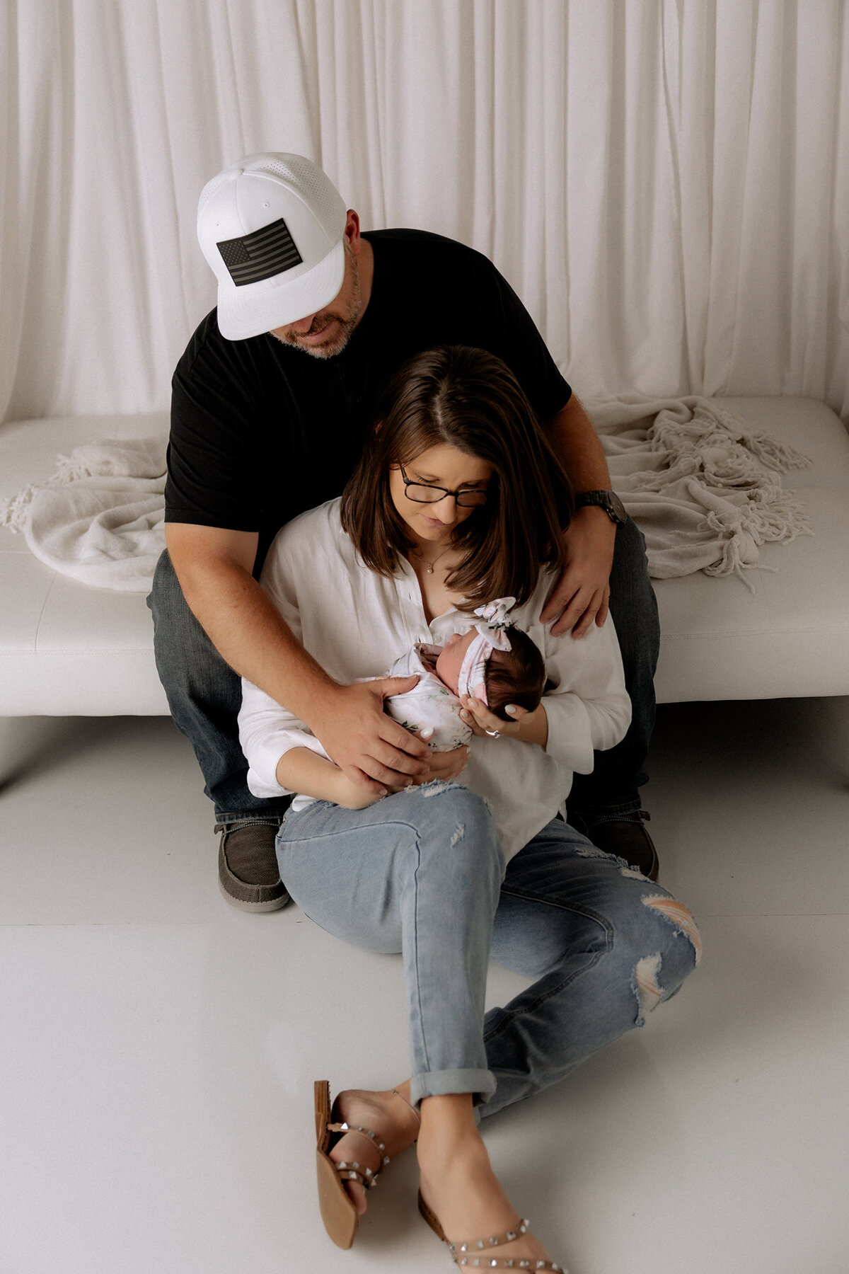 couple with baby girl sitting on floor in front of couch in studio