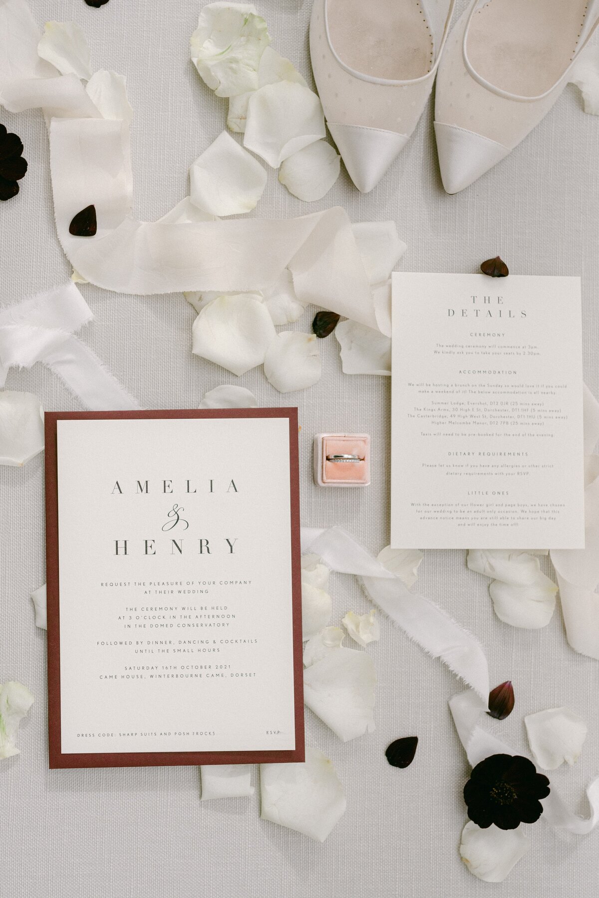 a pastel colour flat lay of wedding details, including invites, rings, petals, satin ribbon and shoes