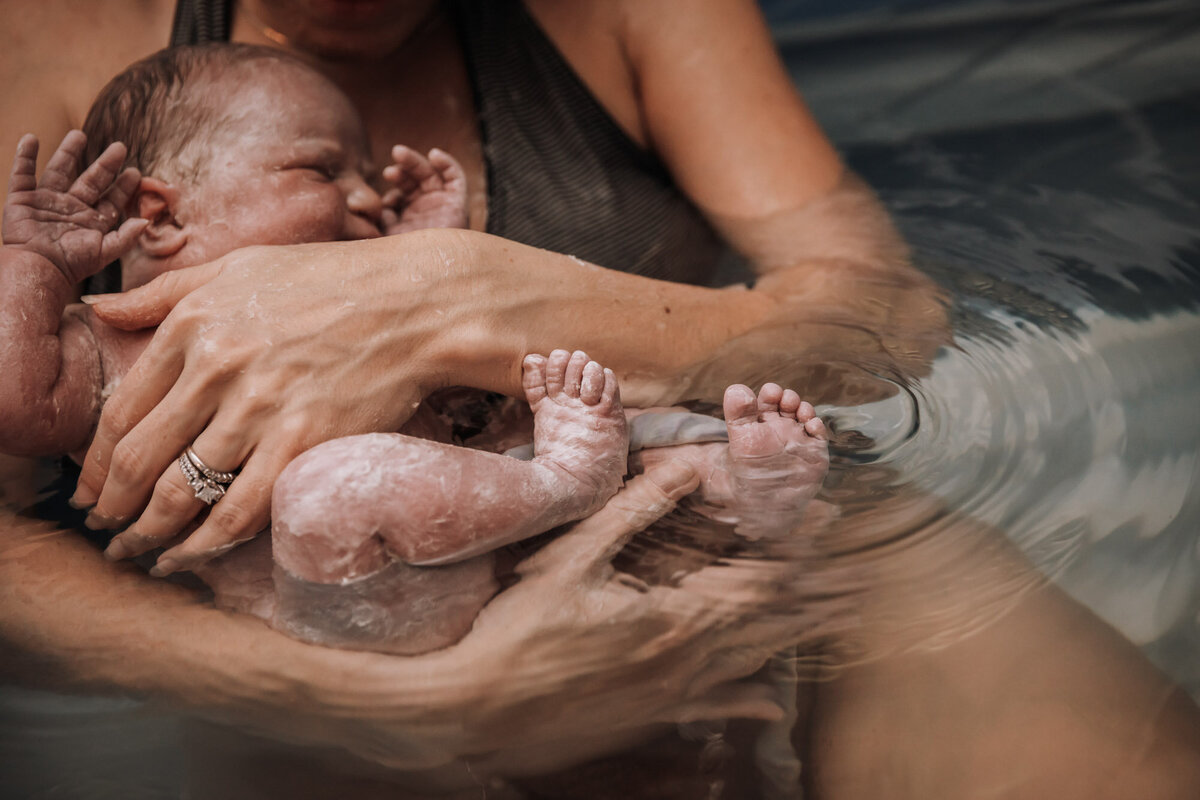woman in birth pool holding newborn