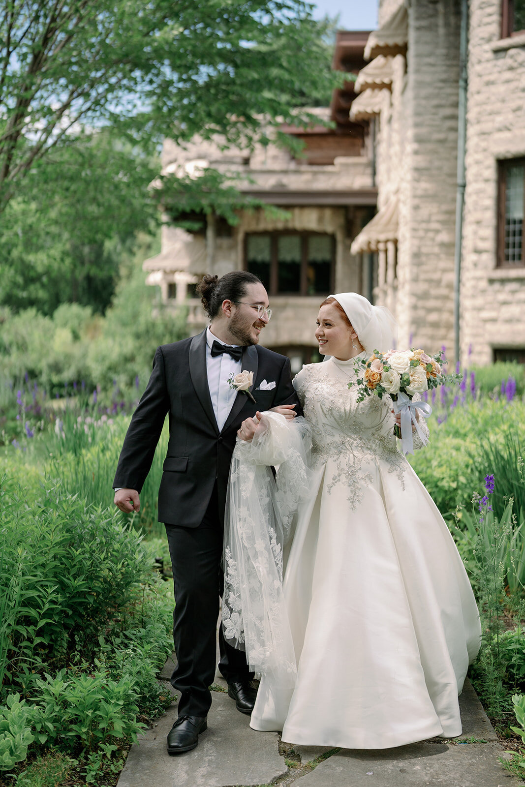 Bride and groom walking outside the stone mansion at Henry Ford Estate in Dearborn Michigan for romantic wedding portraits.