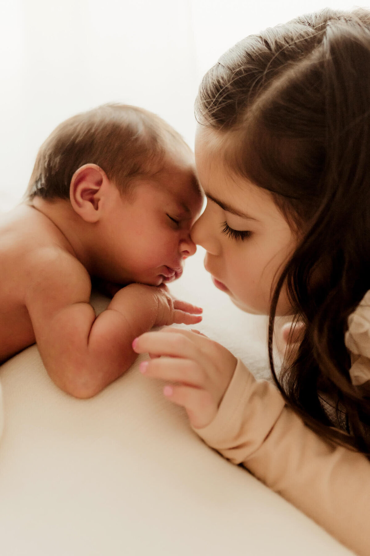 Big sister touches her nose to her baby brother's little nose.