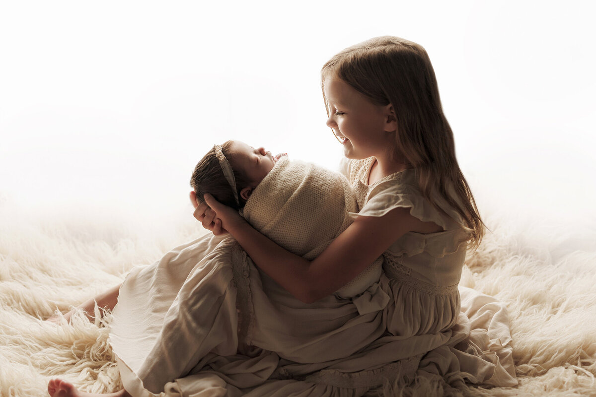 Backlit image of the sweetest sister holding her newborn baby sisiter