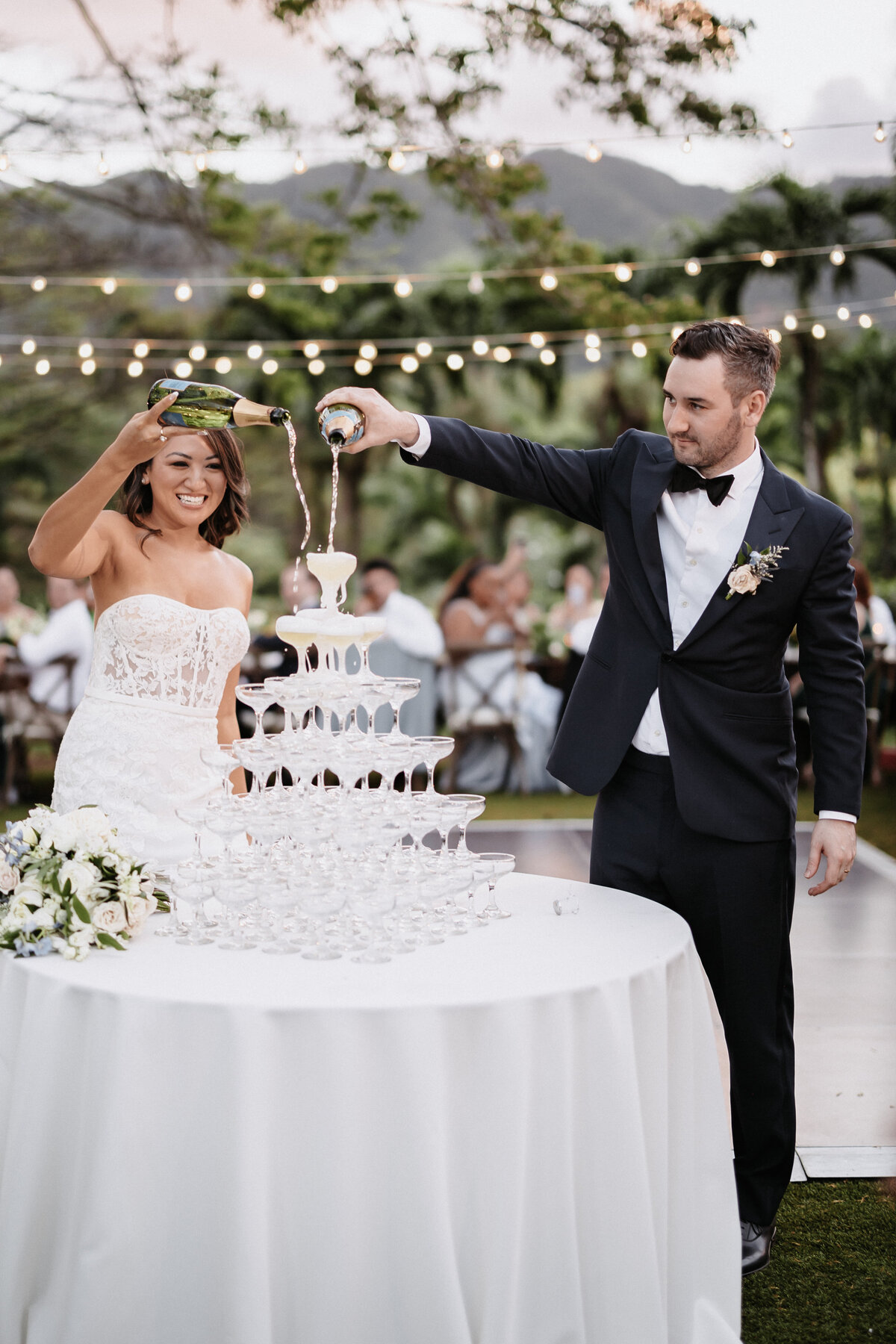 Bride and groom pouring champagne tower in front of their guests