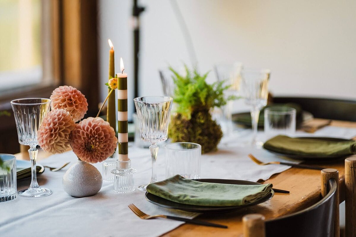 Close of of intimate wedding table decorated with white runner, green napkins, ferns, coral dahlias + candlesticks!