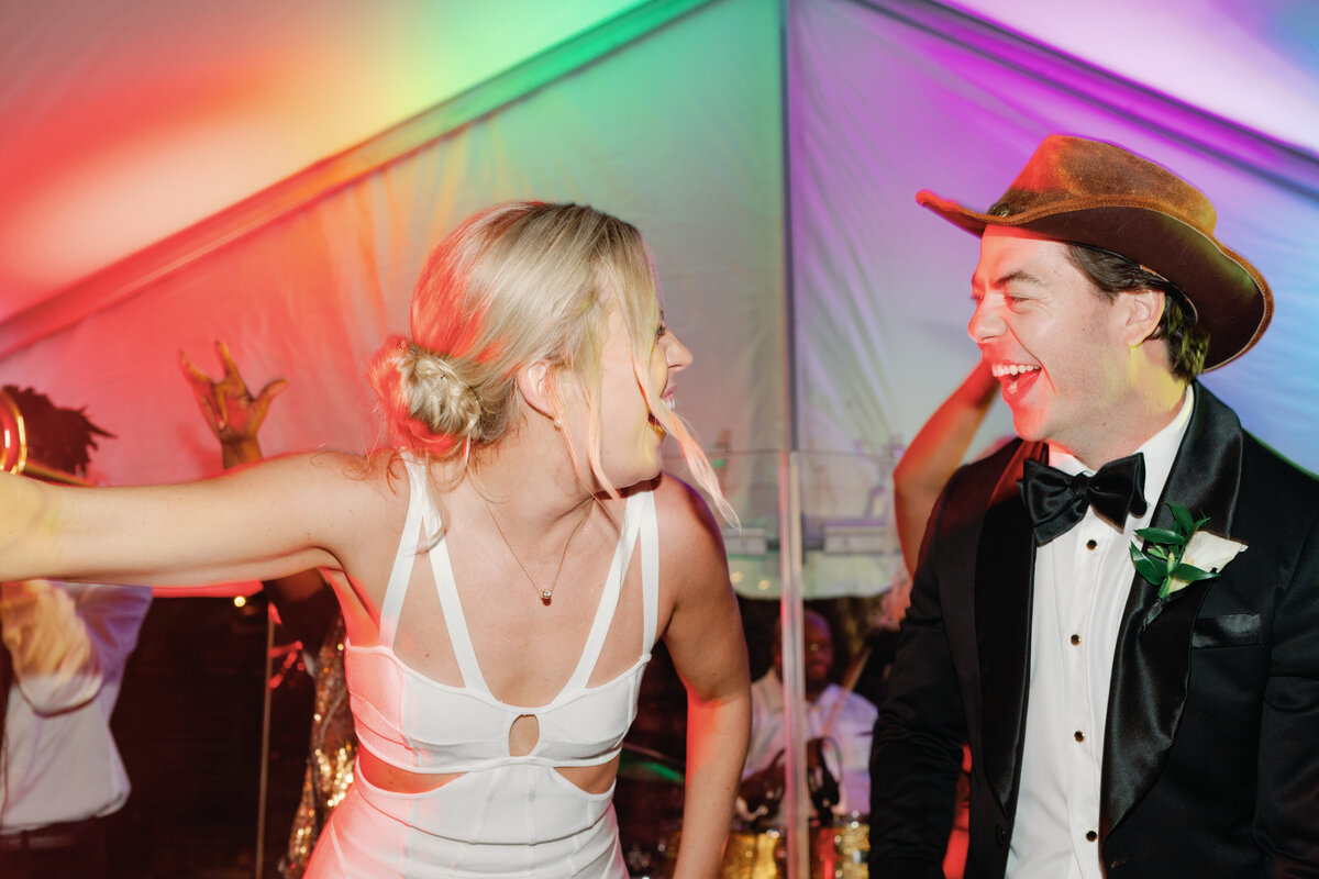 Bride and groom get up on stage with the band. Fun colors and lights at outdoor wedding reception in downtown Charleston.