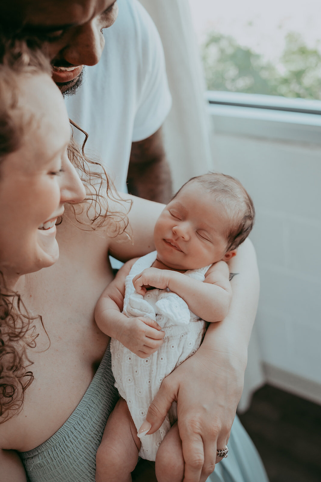 newborn baby girl smiles while parents look at her adoringly