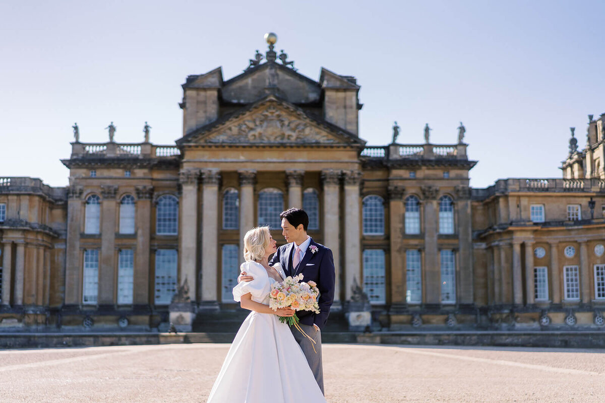 bride and groom embrace and look into each other’s eyes in front of luxury wedding  venue blenheim palace