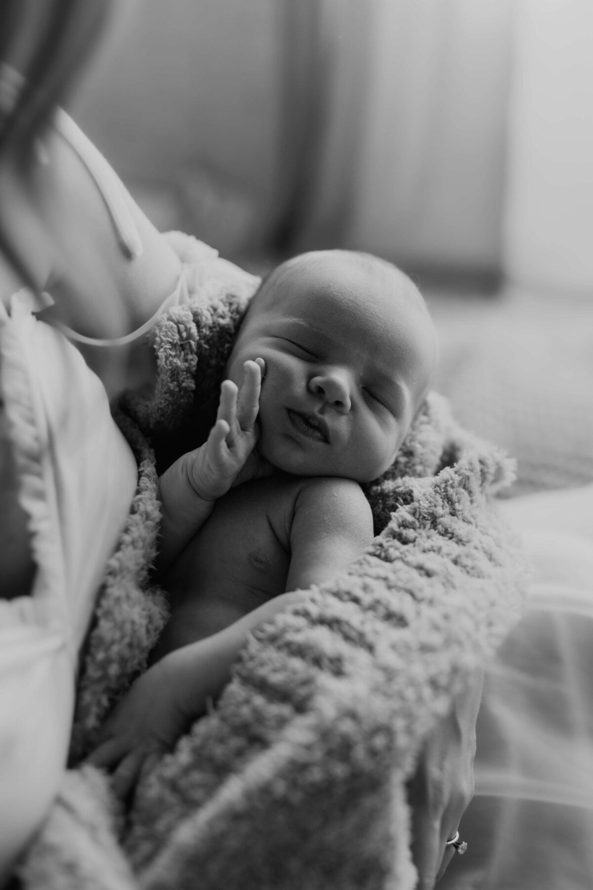 black and whnewborn baby touching his face while mother holds him