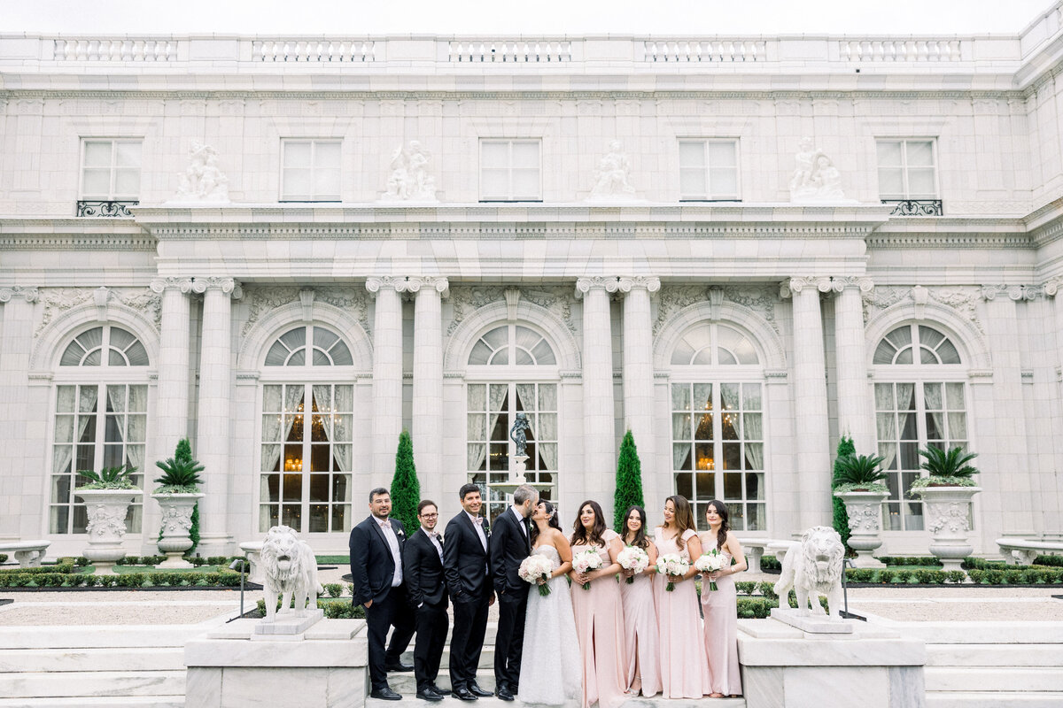 bridesmaids and groomsmen stand on the stairs for candid wedding party portraits in front of rosecliff mansion