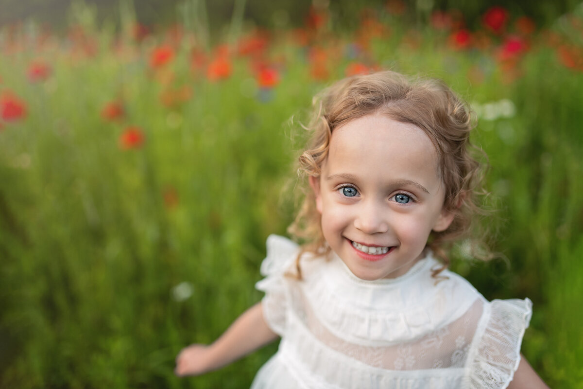 Joyful milestone portrait of a girl in white surrounded by blooming poppies—nature’s perfect frame for her glow.