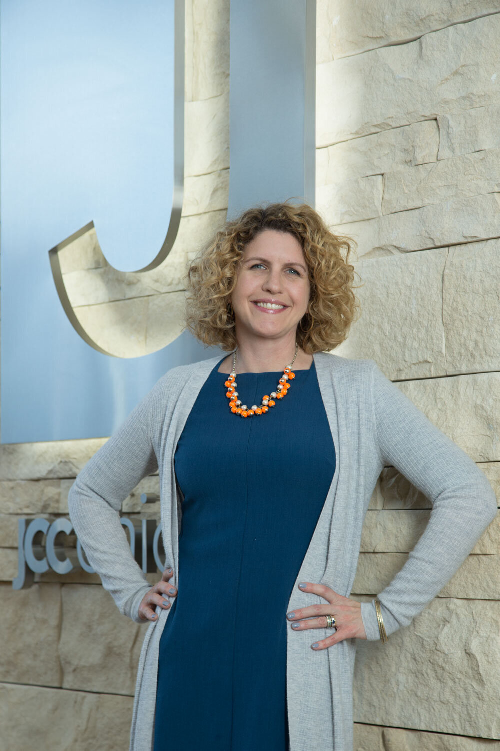Woman in blue dress and gray cardigan smiling outside a building