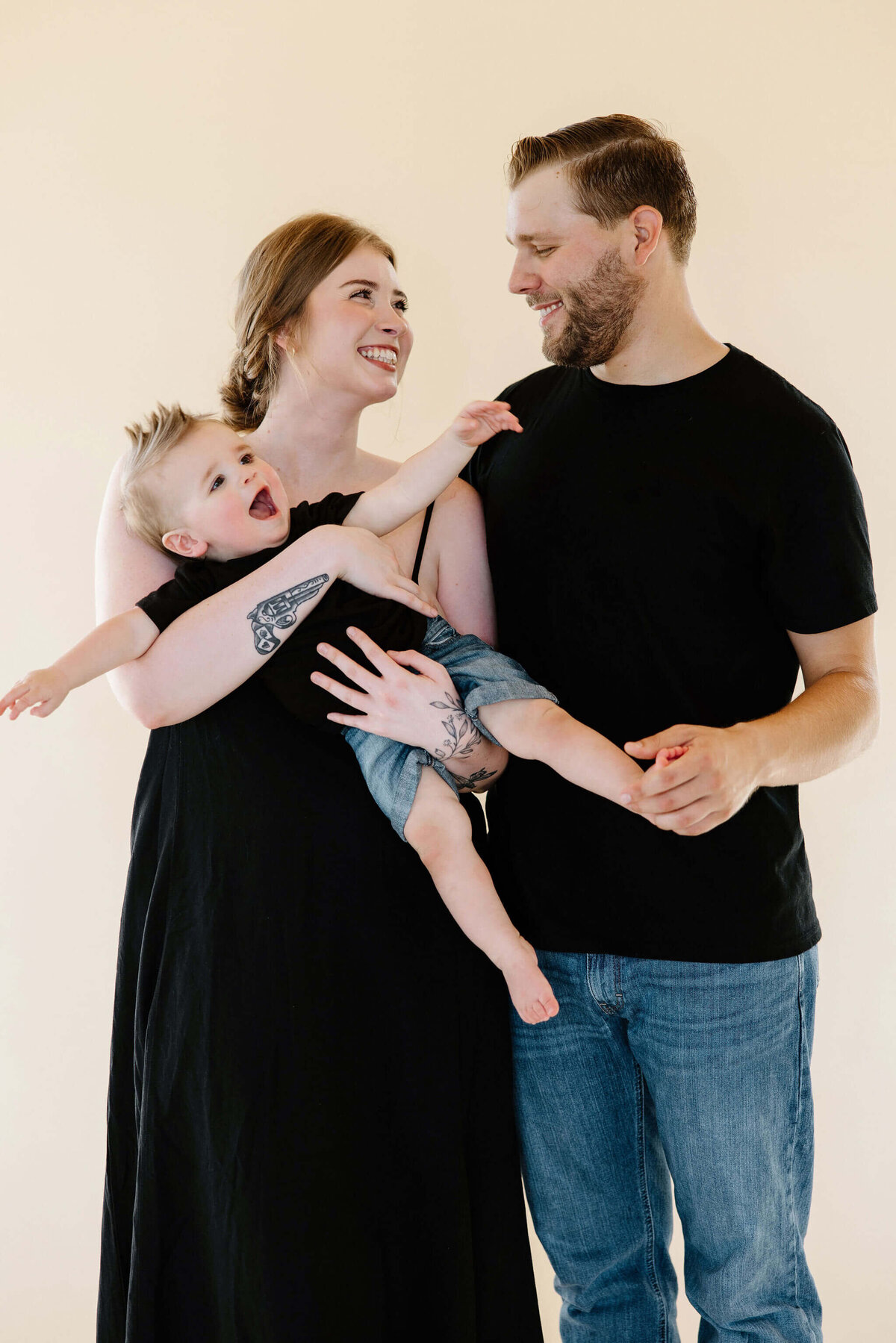 Milestone family pictures with mom and dad playing with 1 year old little boy in photography studio