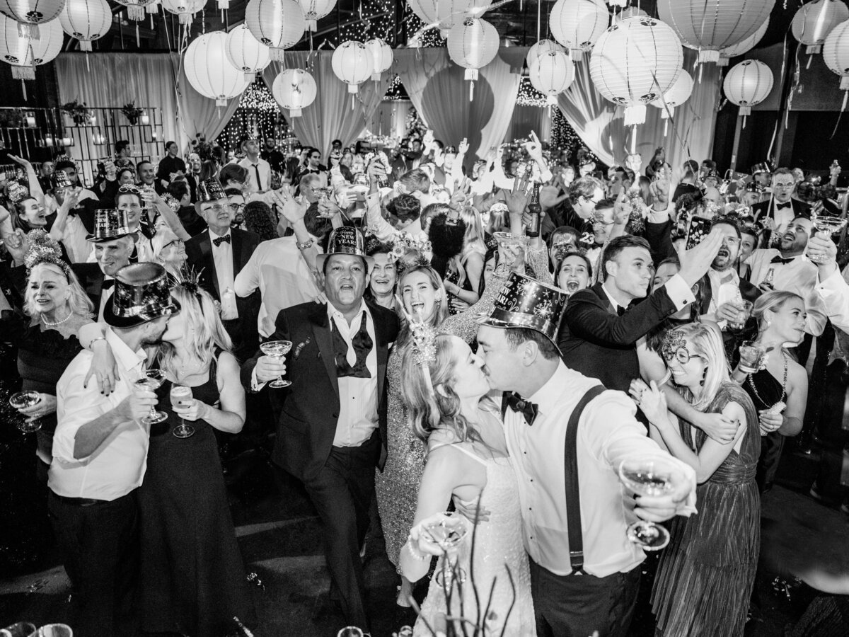Black and white photo of a lively wedding dance floor with guests dancing and celebrating.