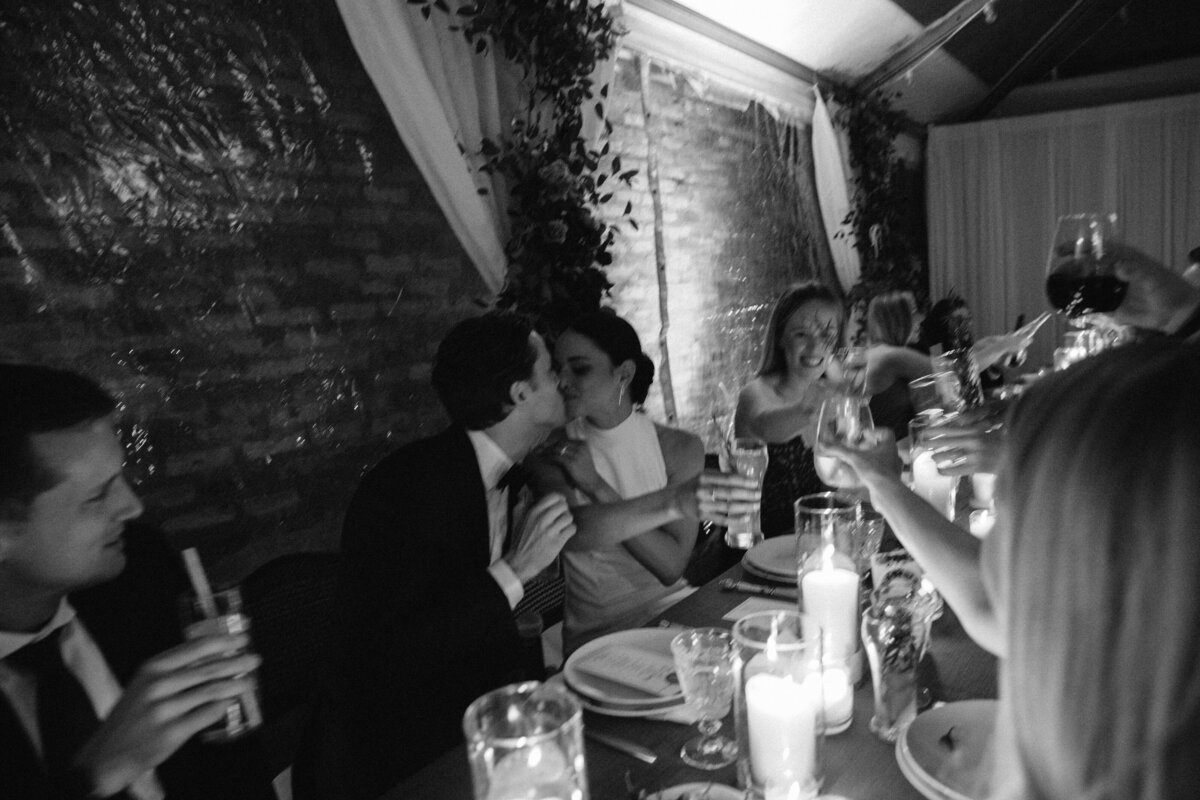Bride and groom share a kiss during speeches of intimate wedding dinner