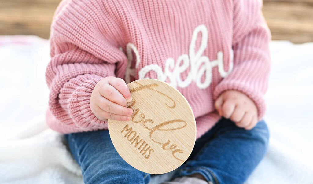 Close up of a baby holding a wooden "twelve months" sign.