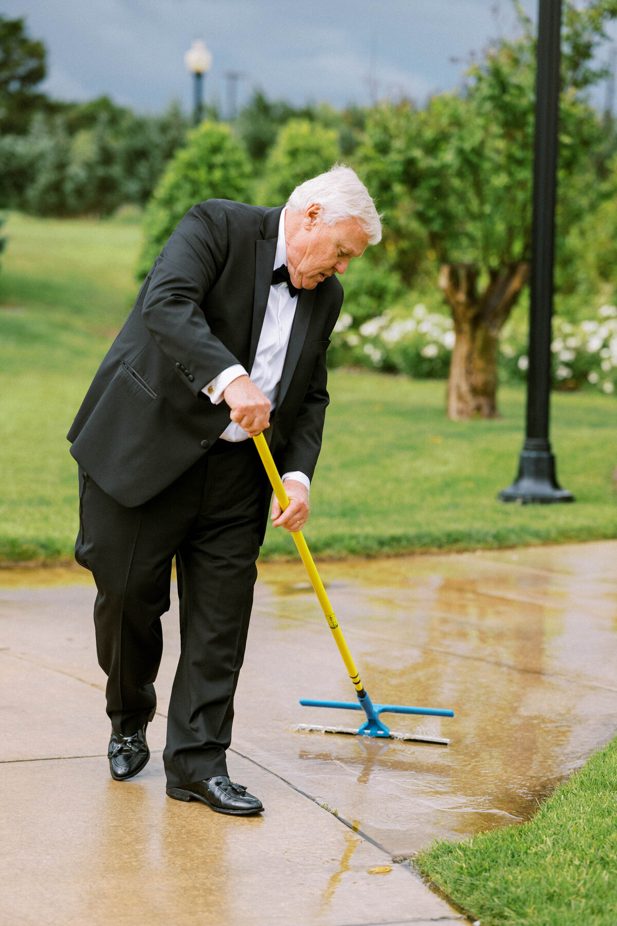 man-in-tuxedo-squeegees-water-off-sidewalk