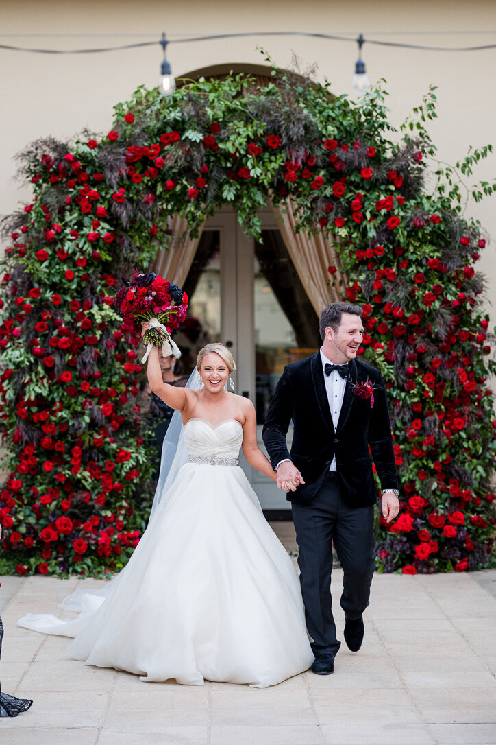 Rounded arch, flower altar, husband and wife, flowers, red roses, garden roses, black, tux, velvet, ballgown, 