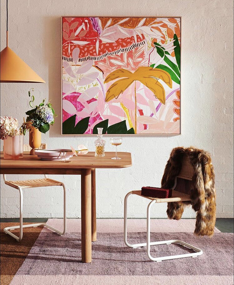 Contemporary dining setup with rattan chairs, timber table and bold botanical artwork styled by interior decorator Melbourne.