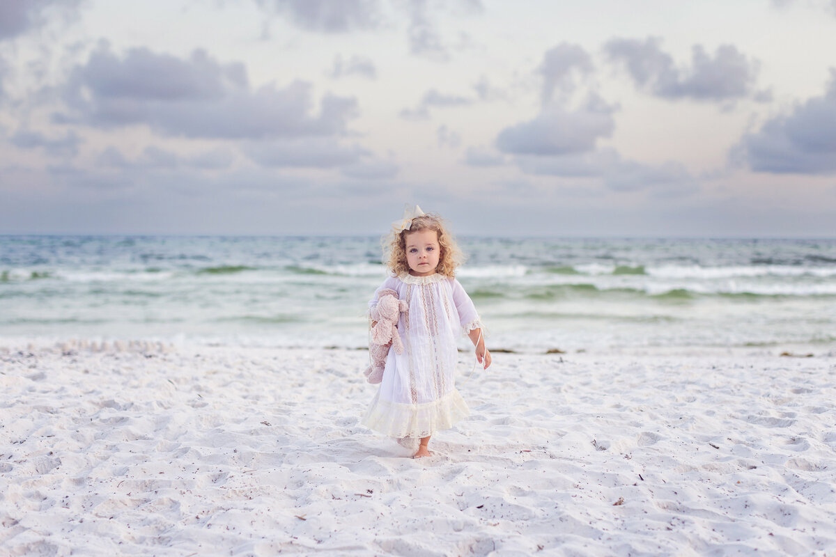 little girl toddler with curls walking on beach with her stuffed animal on 30a