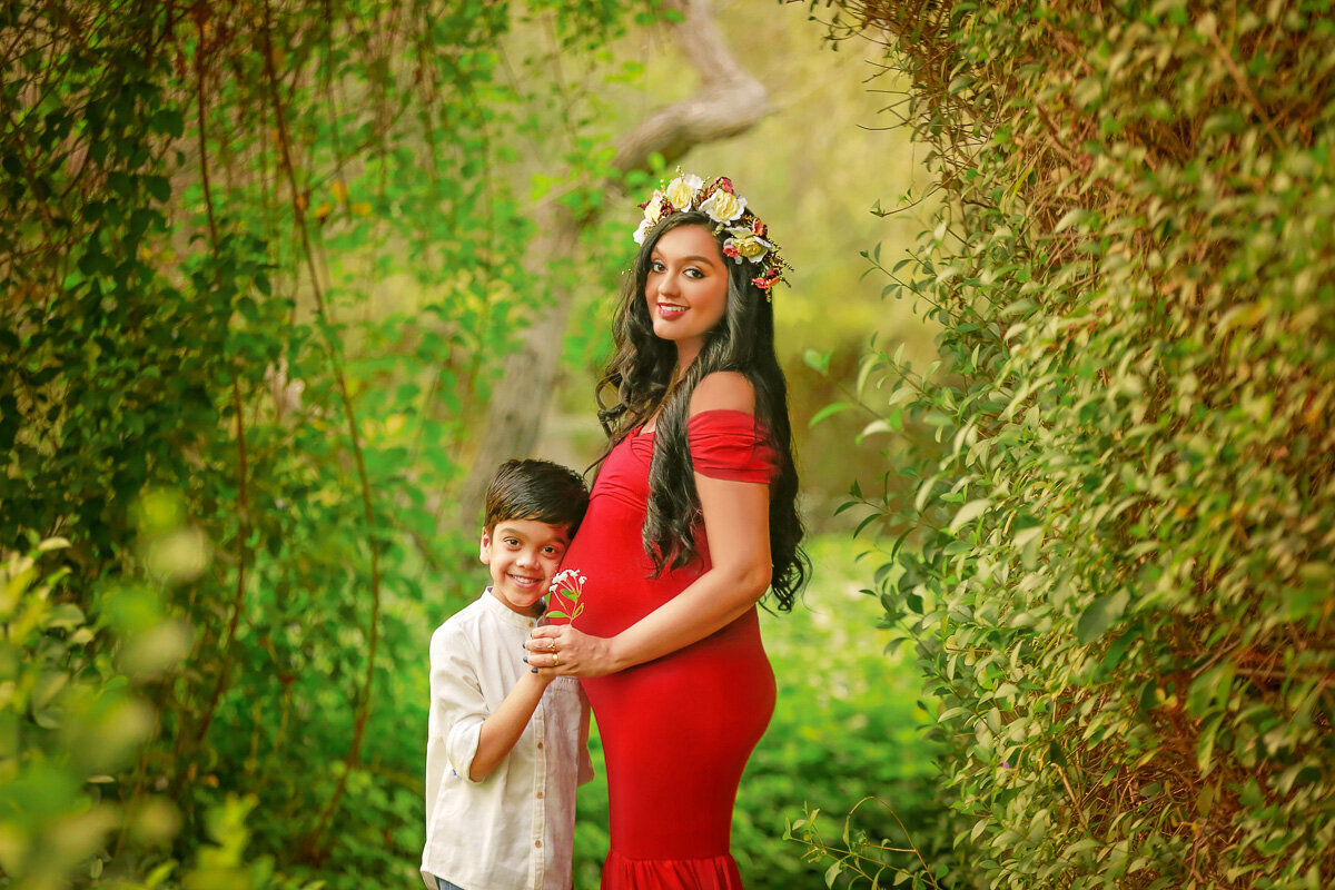 Boy with flowers standing by pregnant mama and holding flowers by Yuliia Terziian Photography