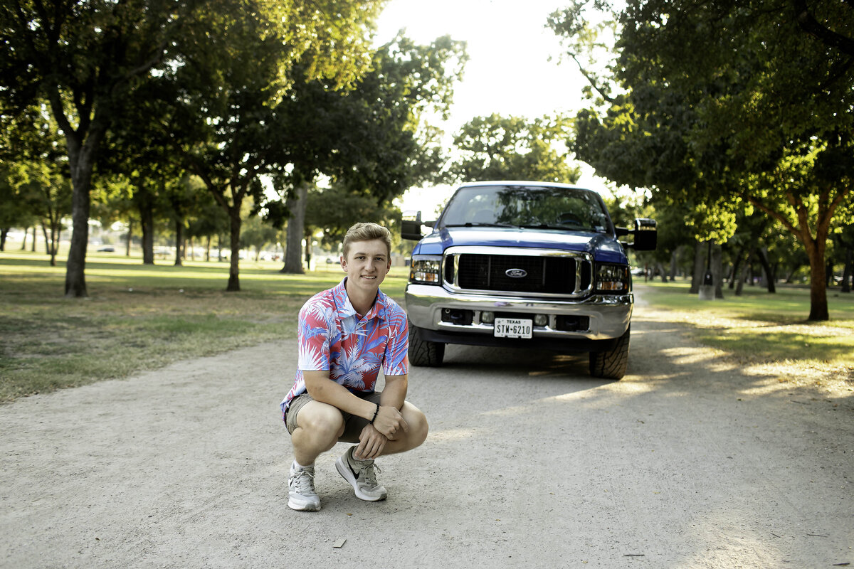 A senior sits on the ground with their legs crossed, casually posing for the camera