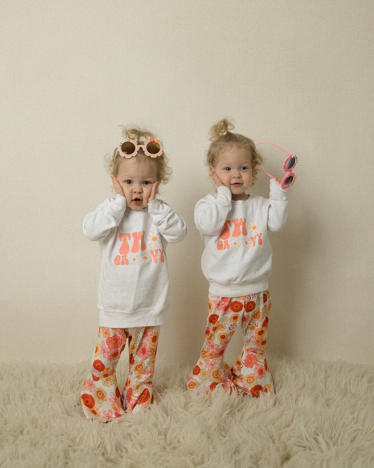 Twin 2 year old girls wearing matching flare pants and sunglasses.