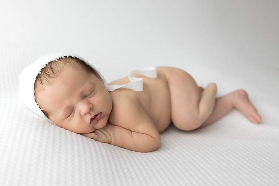 Baby sleeps on a white backdrop during his newborn photos.
