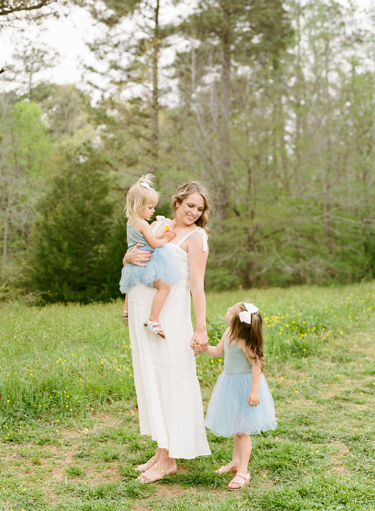 Mom holds daughter's hand while other sits on her belly during a Wake Forest maternity session. Image by Raleigh maternity photographer A.J. Dunlap Photography.