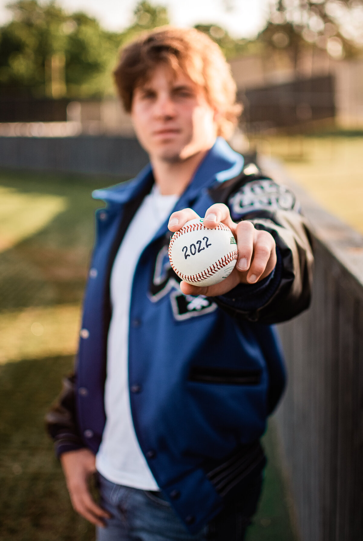 A baseball player at Clear Springs High School wears hit letterman while holding a baseball toward the camera.