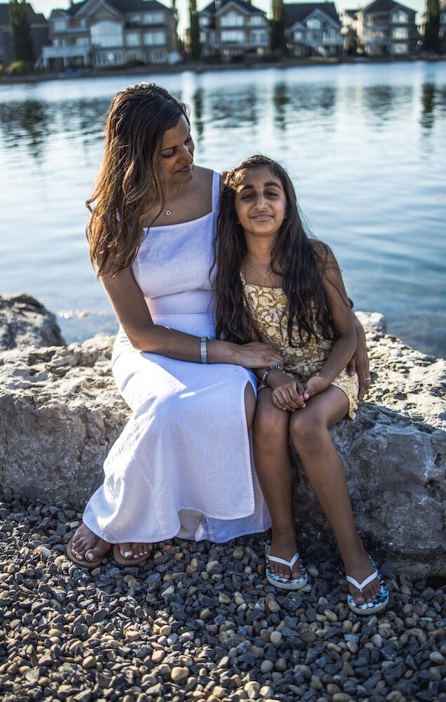 A mom and daughter sit side by side on a rock by the lake