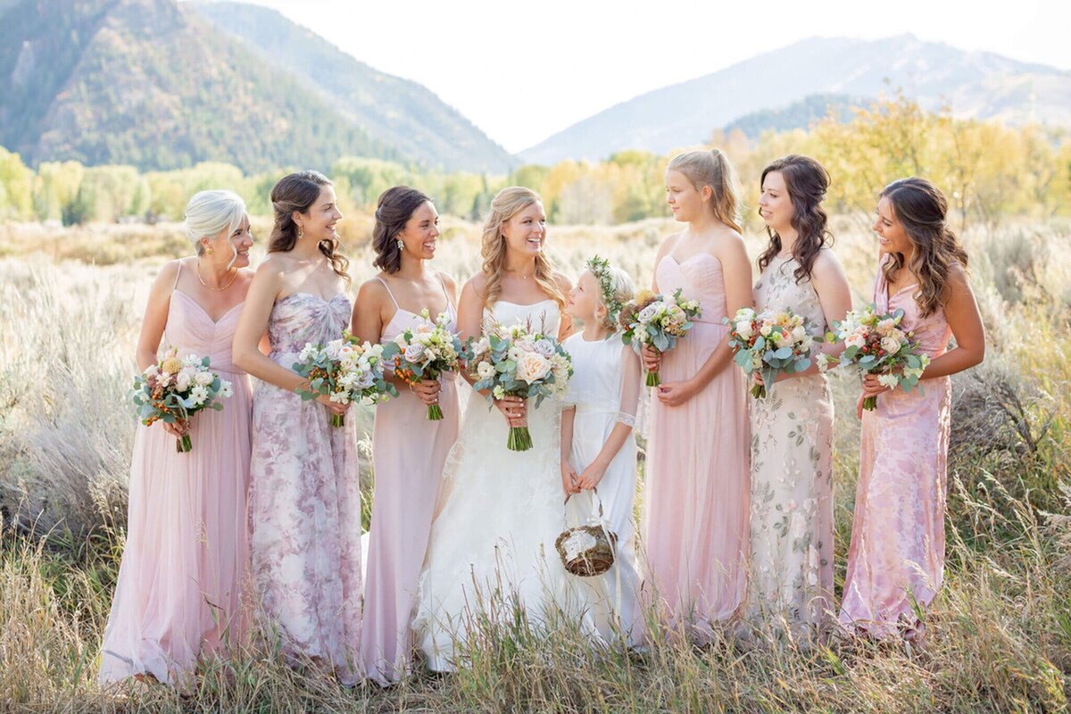 A bride and her six bridesmaids in blush pink dresses pose for a photo in front of Shadow Mountain, in Aspen, CO.