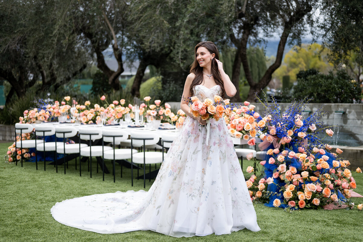 San Francisco Bay Area wedding photographer captures elegant bridal portrait with flowing gown against colorful floral installation and natural vineyard landscape at Estate Yountville in Napa Valley