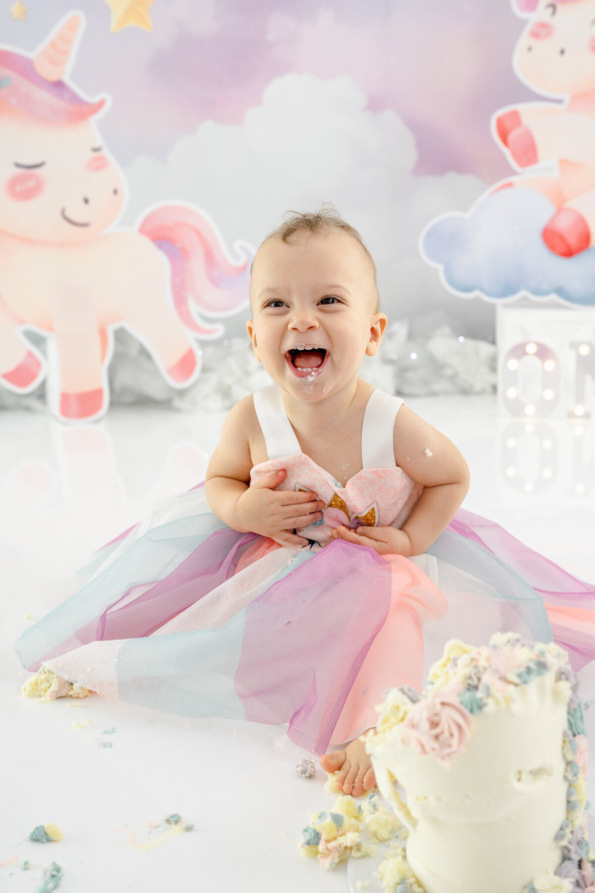 Girl in unicorn dress eating unicorn cake during themed cake smash session— captured by Alliston and Barrie cake smash photographer.