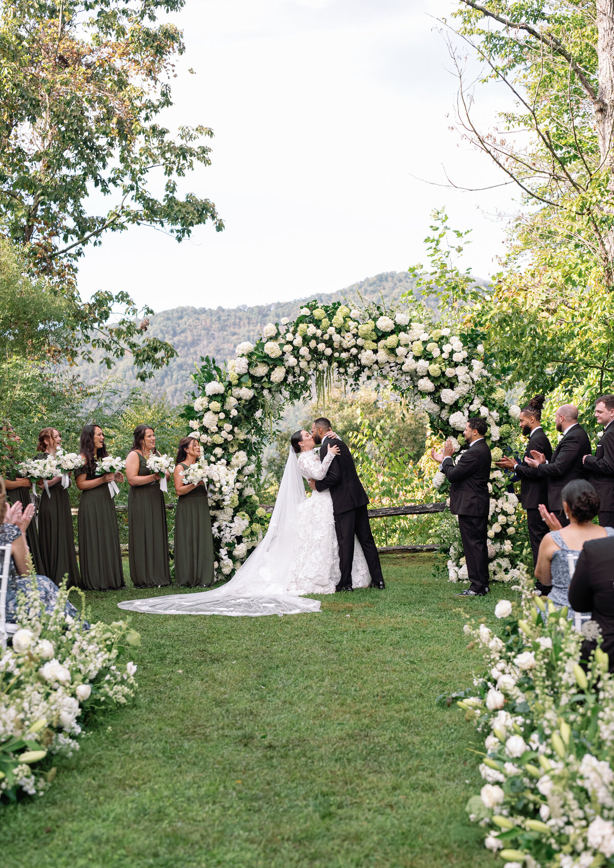 Bride and groom sharing their first kiss under a white floral arch with mountain views at Castle Ladyhawke.