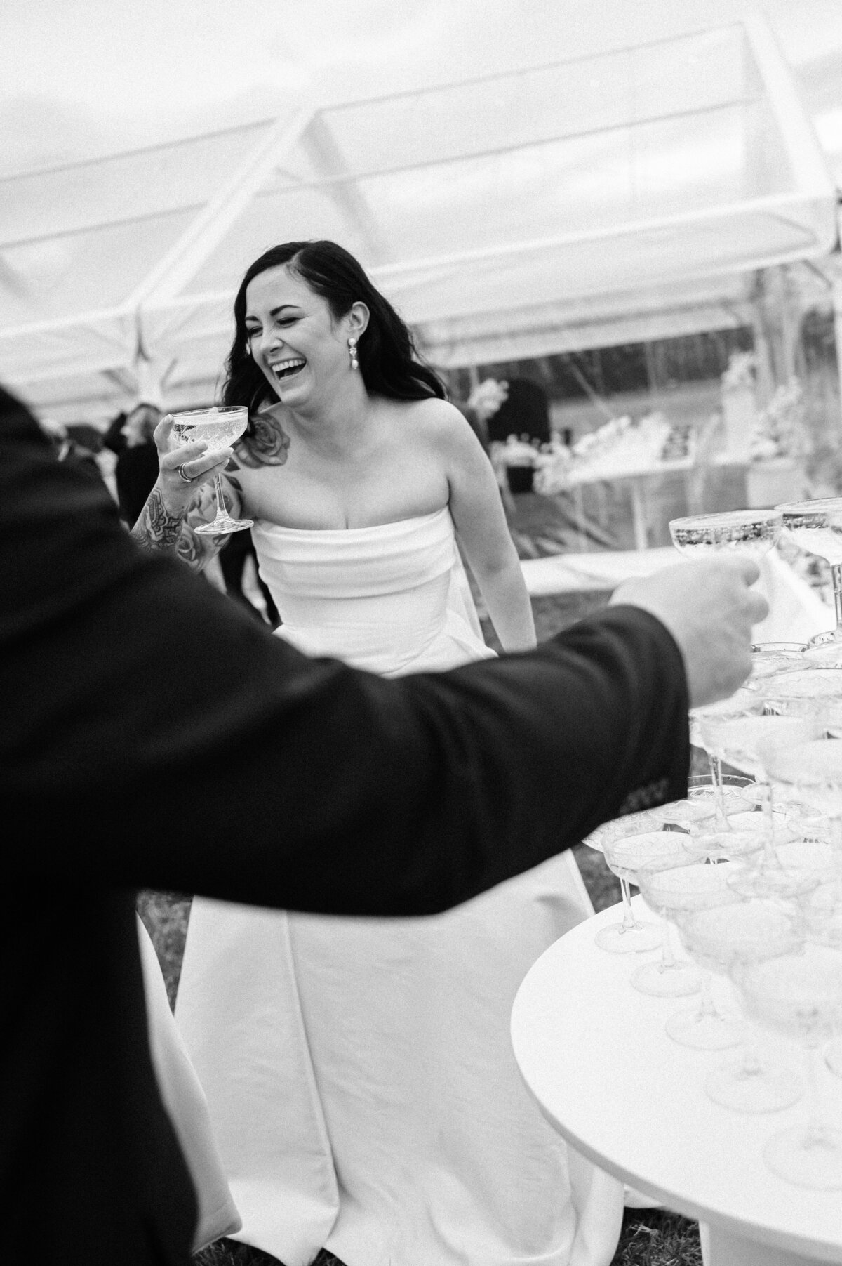 candid photo of a bride laughing with a glass of champagne by a champagne tower