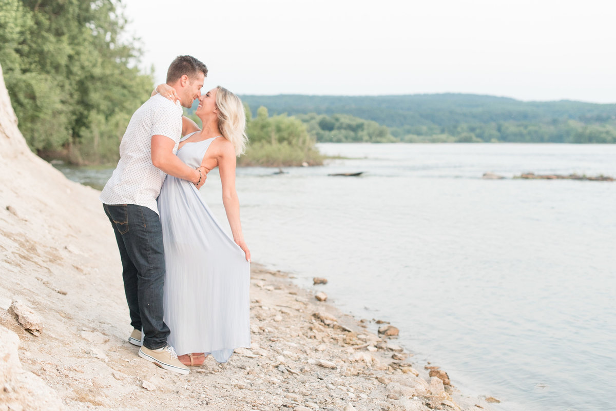 Engaged couple almost kissing as she fans out her dress along the shoreline of the Susquehanna River at the White Cliffs of Canoy.