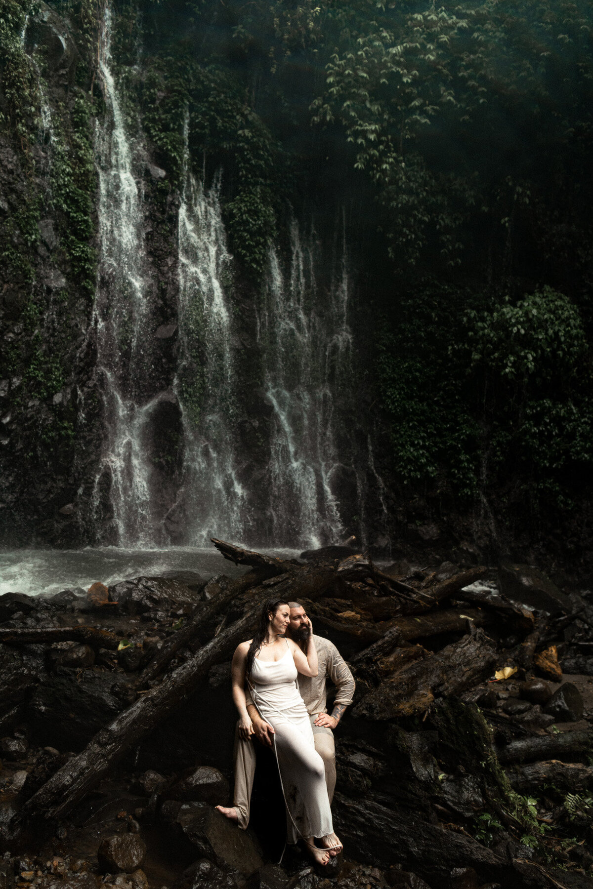 An adventurous bride and groom sit underneath a waterfall at their Costa Rica elopement.