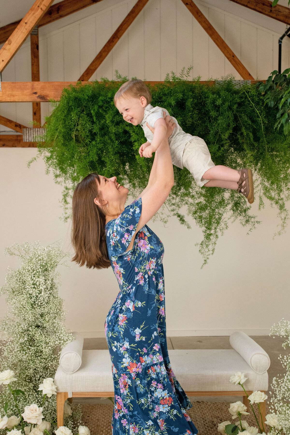 happy mother holds toddler up in the air playfully while he smiles