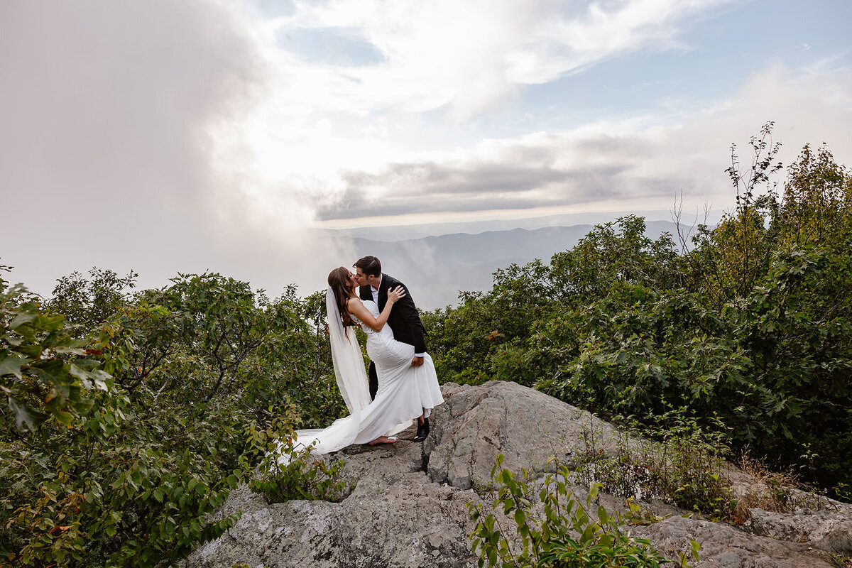 Newlyweds kissing on a boulder in the mountains