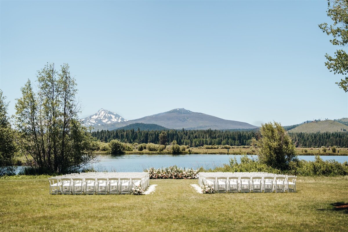 Pastel ground ceremony arch and white chairs in front of lake facing mountains at Black Butte Ranch