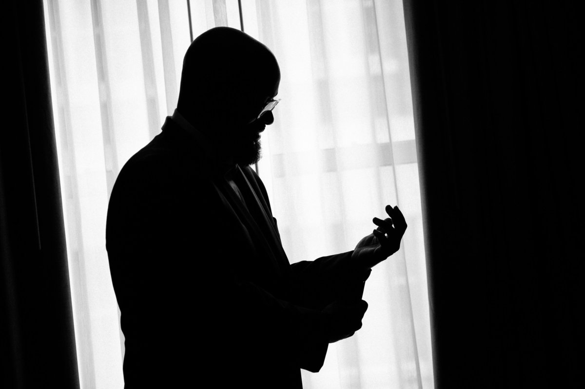 Silhouette of groom as he attaches his cuff links and finished getting ready for his wedding.