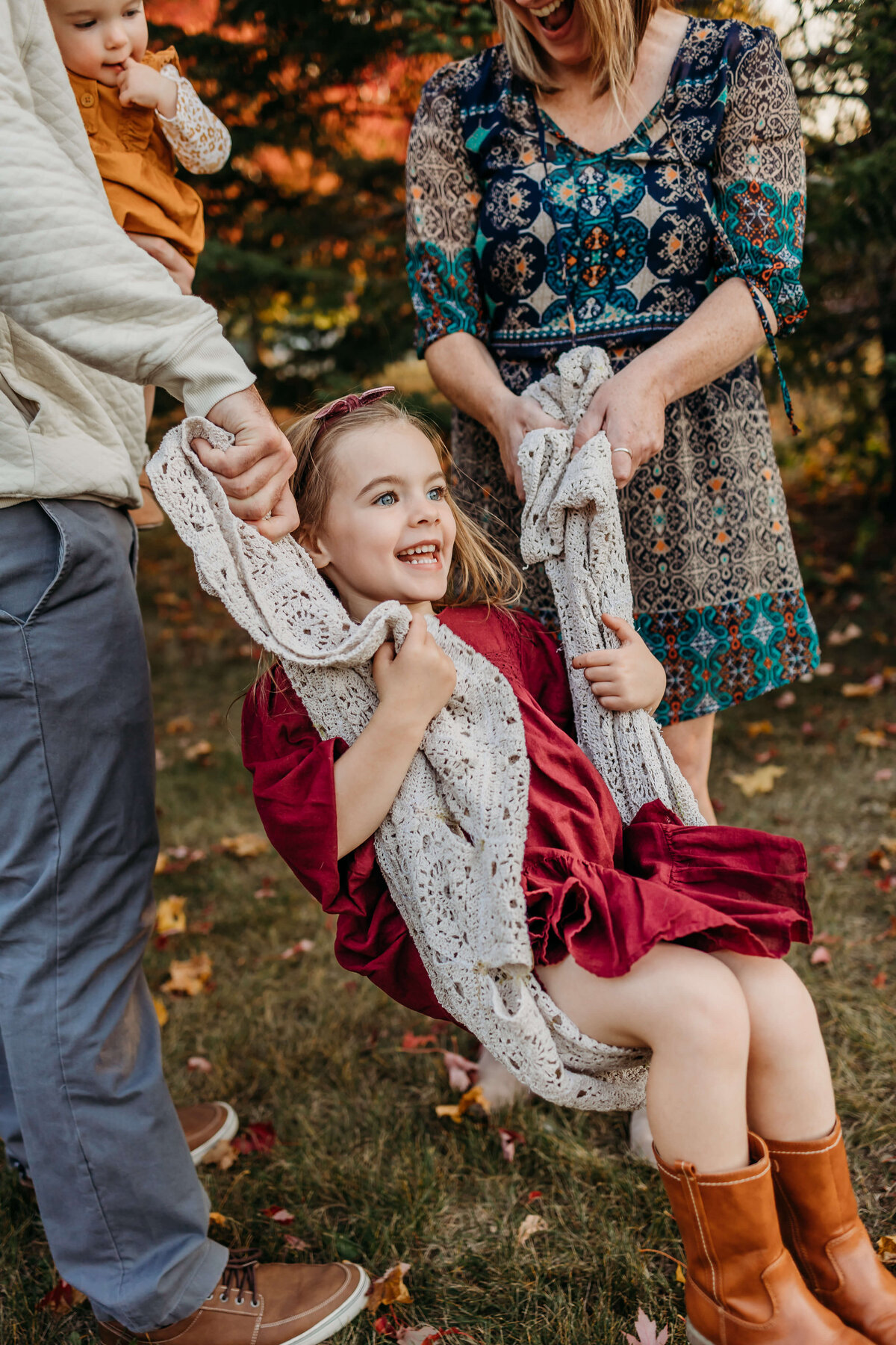 girl swinging on blanket held by parents family session