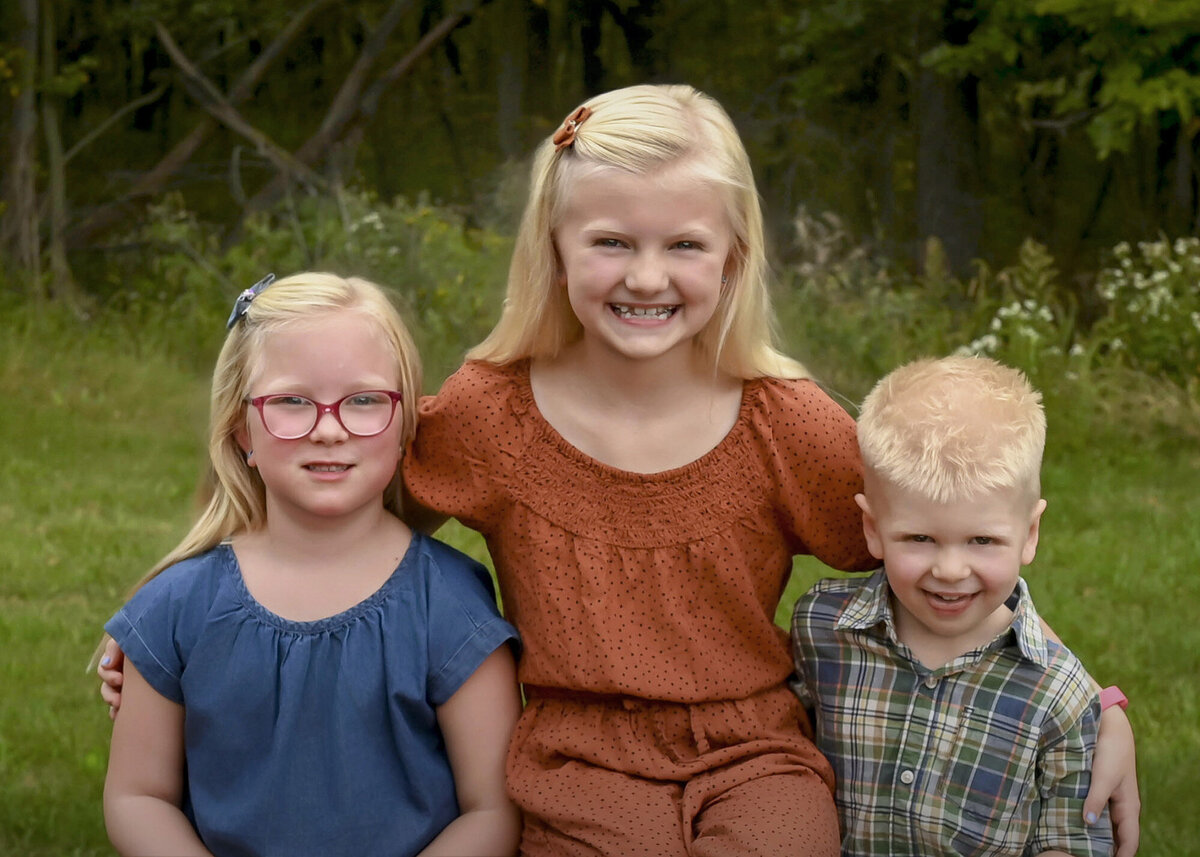 A boy and his 2 sisters sit together and smile