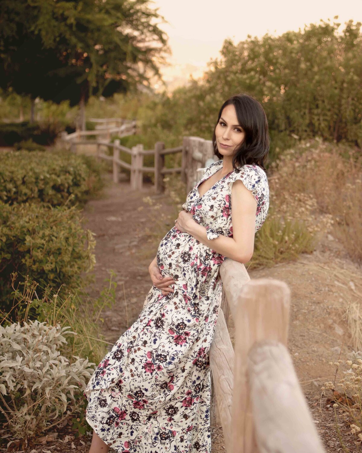 Expectant mom holding bump leaning against a wood fence in Elsinore Mountain Park.