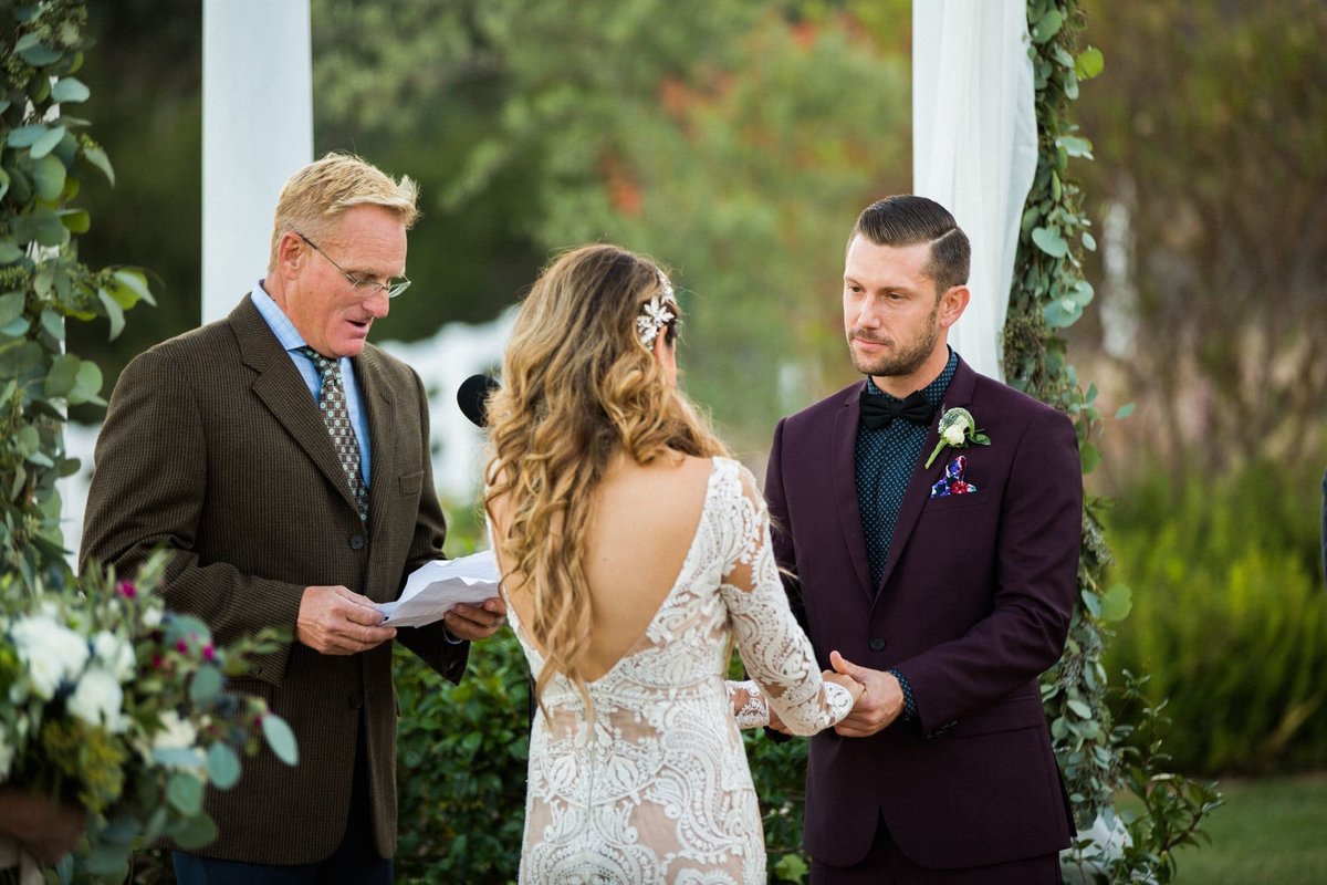 Groom takes his Bride's hand as the officiant reads the wedding vows