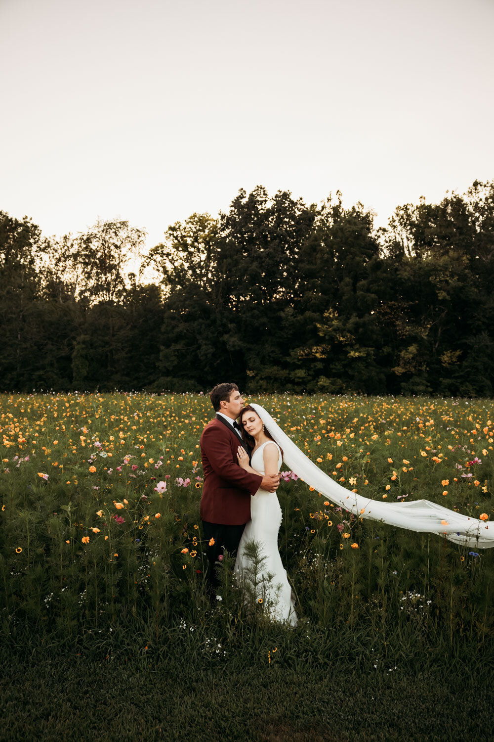 Bride and groom embracing in a wildflower meadow at dusk