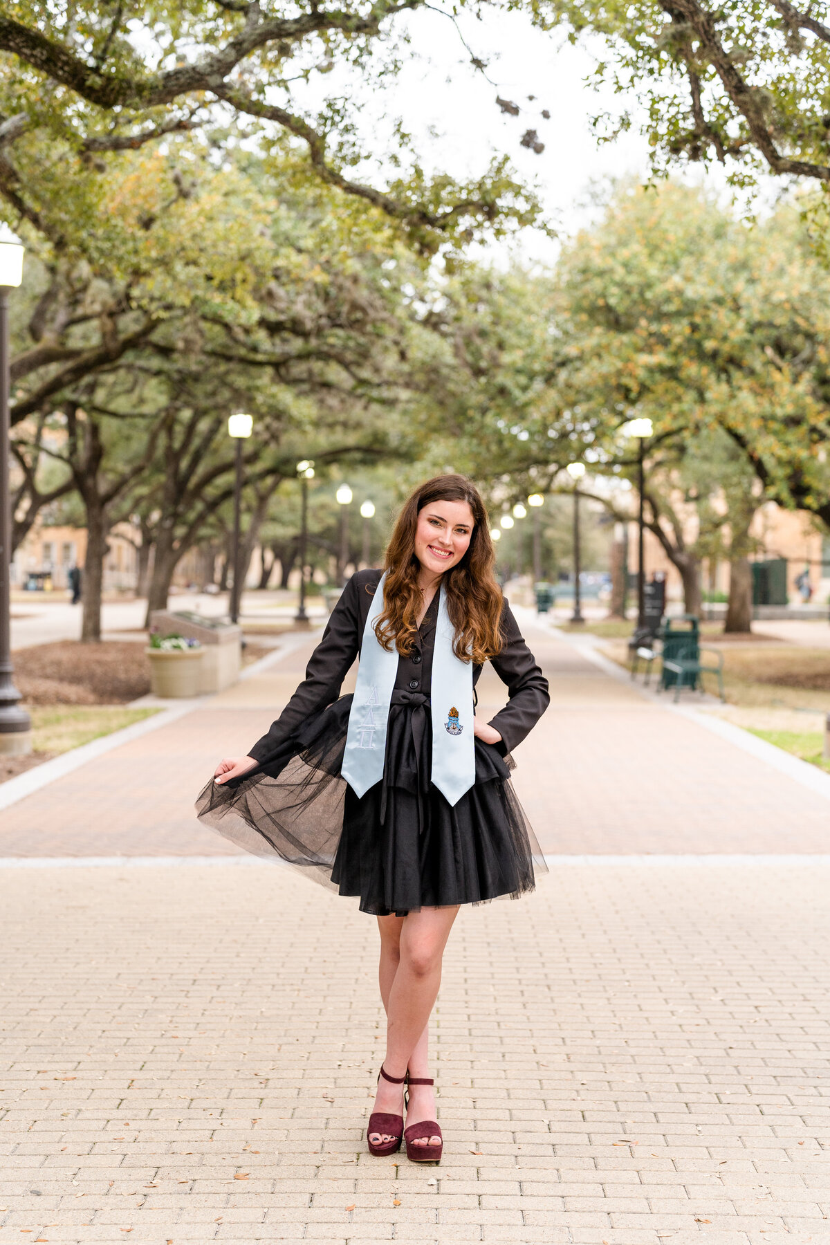 Texas A&M senior girl fluffling black dress and smiling while wearing Pi Phi stole in Military Plaza